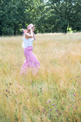 Young beautiful girl with pink hair in the summer hat walking in the golden field