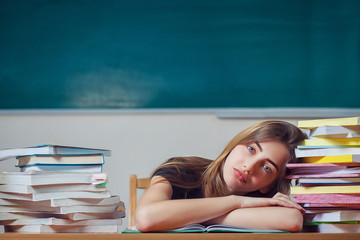 Pretty female student with books working in a classroom. Tired blonde student on her desk with many books. Education, school and university concept. Copy space