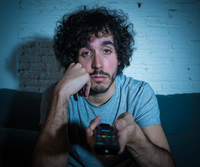 Portrait of bored sleepless young man sitting on the couch watching TV at night