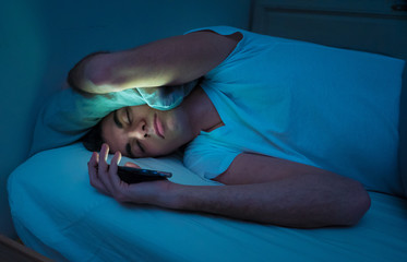 Young man addicted to online social media sleepless surfing on the Internet in bed - obrazy, fototapety, plakaty
