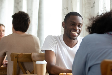 Happy smiling black guy sitting in coffeehouse with friend.