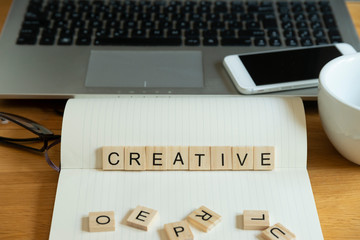 Concept keyword creative in wooden tile letters  in personal home desk setting with laptop,...