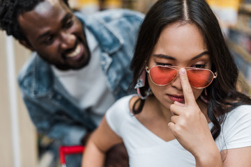 Selective focus of Asian woman touching sunglasses near happy African American man