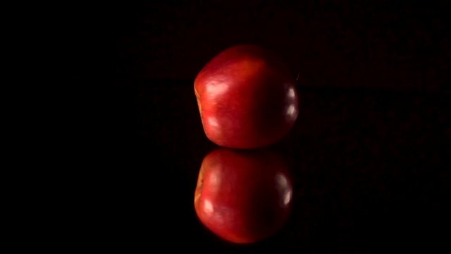 Fresh red apple rotating and rolling on a black mirror table. Black background.