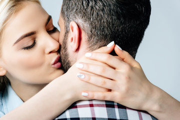 beautiful blonde girl kissing and embracing man isolated on grey