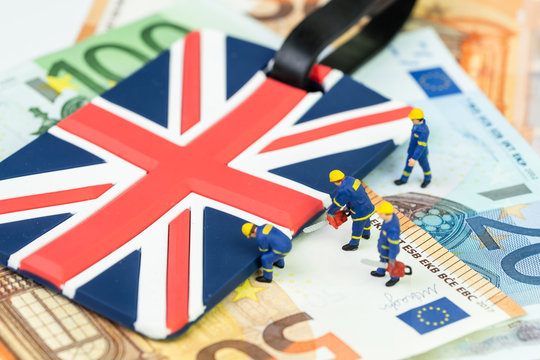 Brexit withdrawal plan or Euro zone departure concept, miniature figures worker help cut and move UK Union jack flag from pile of Euro banknotes money