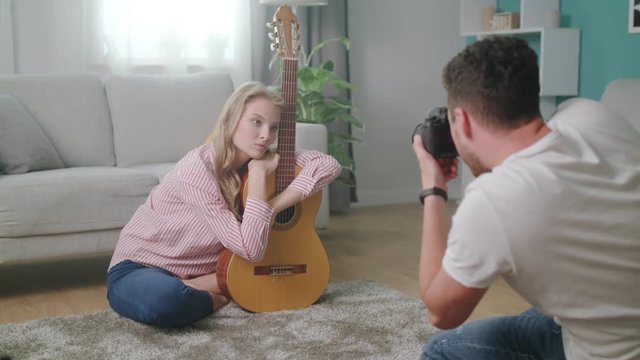 A young man photographs a girl with a guitar at her home