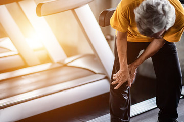 Elderly man having pain in his knee at the gym