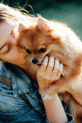 Smiling woman hugging pomeranian spitz-dog outdoor at the mountain in a sunny summer day