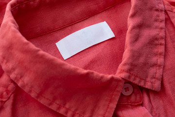 White blank clothing tag label on red linen shirt fabric texture background