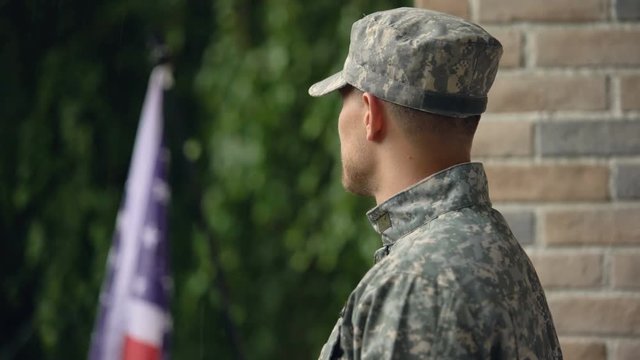 Happy soldier glad to return back home, standing on backyard of house, rain