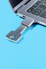 USB-drive in the form of a key through the adapter connected to a modern laptop on a blue background. Vertical.