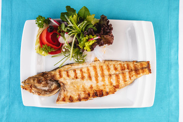 Mediterranean dish, European cuisine. Rainbow trout, grilled, served with vegetables - tomato, lettuce, radish, iceberg cabbage