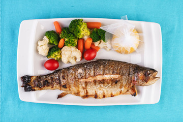 Mediterranean dish, European cuisine. whole fish baked in the oven, served with steamed vegetables - cauliflower, broccoli, carrots, cherry tomatoes and lemon
