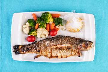 Mediterranean dish, European cuisine. whole fish baked in the oven, served with steamed vegetables - cauliflower, broccoli, carrots, cherry tomatoes and lemon