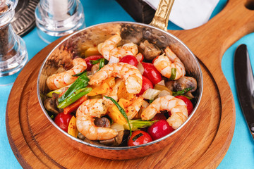 Seafood, Mediterranean cuisine, European dish. Warm salad of grilled fish pieces, shrimps and mussels in a frying pan, with grilled vegetables - with green onions, greens, mushrooms and vegetables.