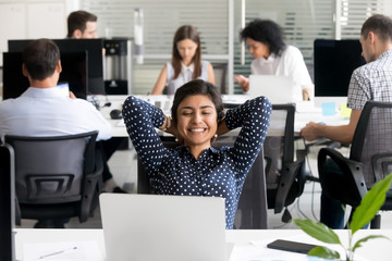 Smiling Indian female employee relaxing leaning back at workplace