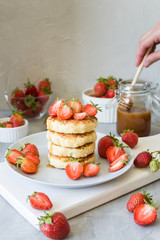 Cottage cheese pancakes syrniki with strawberries and honey. The concept of tasty healthy summer Breakfast. Spoon for honey in hand. Copy space, side view.