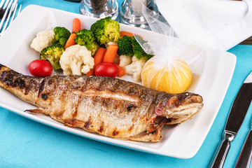 Mediterranean dish, European cuisine. whole fish baked in the oven, served with steamed vegetables - cauliflower, broccoli, carrots, cherry tomatoes and lemon
