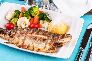 Mediterranean dish, European cuisine. whole fish baked in the oven, served with steamed vegetables - cauliflower, broccoli, carrots, cherry tomatoes and lemon