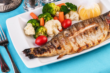 Mediterranean dish, European cuisine. whole fish baked in the oven, served with steamed vegetables - cauliflower, broccoli, carrots, cherry tomatoes and lemon