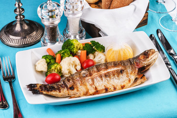 Mediterranean dish, European cuisine. whole fish baked in the oven, served with steamed vegetables - cauliflower, broccoli, carrots, cherry tomatoes and lemon
