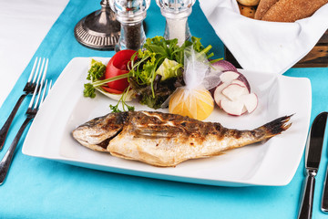 Mediterranean dish, European cuisine. whole fish baked in the oven, served with a salad of vegetables, greens, arugula, onion rings, tomato and lemon