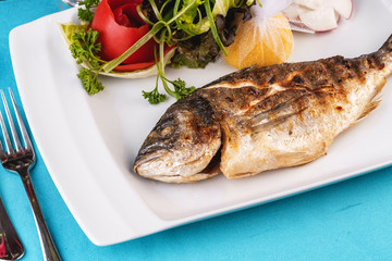 Mediterranean dish, European cuisine. whole fish baked in the oven, served with a salad of vegetables, greens, arugula, onion rings, tomato and lemon