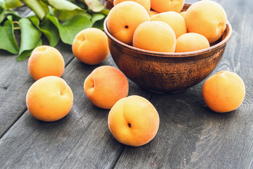Delicious ripe apricots in a bowl next to green leaves on a wooden table.