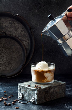 Female hand pouring coffee on vanilla ice cream to make an affogato coffee. Summer coffee drink with ice cream and espresso in the glass