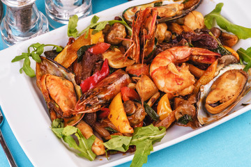 Mediterranean dish, European cuisine. Braised shrimps, mussels, squids with vegetables, red and green pepper, tomatoes, greens, arugula and mushrooms