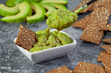 Guacamole in a bowl on a background of sliced avocado.