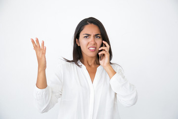 Annoyed beautiful woman speaking on phone. Angry young Latin woman in white shirt making displeased face and gestures and talking on cell. Feeling stressed concept