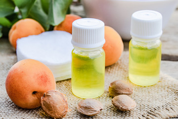 Apricot oil in a small jar near ripe yellow apricot on a wooden table.