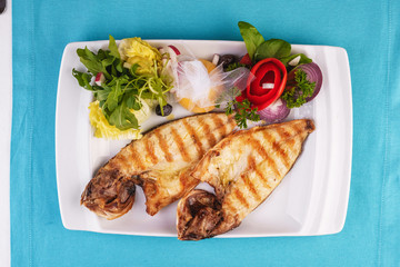 European cuisine, Mediterranean dish. River trout steak, white meat fish, served with vegetables, lemon and arugula and tomato salad