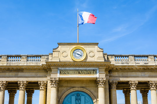 Close-up view of the pediment with clock and french flag of the southern entrance of the Palais Bourbon, seat of the French National Assembly (Assembl&eacute;e Nationale) in Paris, France, on a sunny day.