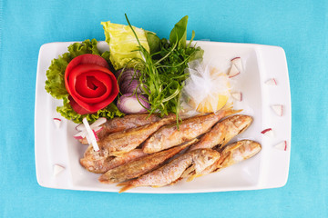 European cuisine, Mediterranean dish. Fried fish in deep fat, capelin in batter with greens, tomatoes, cheese and red onion