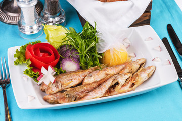 European cuisine, Mediterranean dish. Fried fish in deep fat, capelin in batter with greens, tomatoes, cheese and red onion