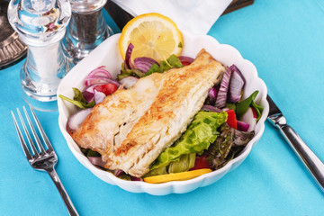 Mediterranean dish, European cuisine. grilled white fish steak on a pillow of lettuce- lemon, arugula, red onion rings, lettuce leaves, cabbage, tomatoes with olive oil