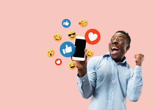 Social media interactions on mobile phone. Internet digital marketing, Chating, commenting, liking. Smiles and icons above smartphone screen, that holding by young man on pink studio background.