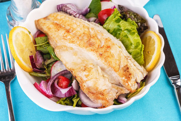 Mediterranean dish, European cuisine. grilled white fish steak on a pillow of lettuce- lemon, arugula, red onion rings, lettuce leaves, cabbage, tomatoes with olive oil