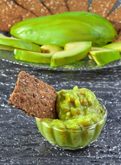 Guacamole in a beautiful bowl with crispy loaves on the background of sliced avocado. Vertical.
