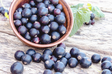 Black currant lies next to the green leaves on a wooden background. Juicy natural fruits currant.