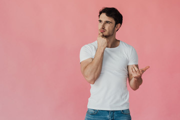 pensive muscular man in white t-shirt propping face with fist and counting on fingers isolated on...