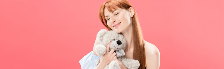 panoramic shot of smiling redhead young woman holding teddy bear with closed eyes isolated on pink