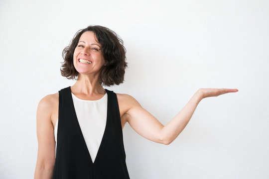 Joyful Excited Woman In Casual Presenting Information. Middle Aged Business Lady Standing Over White Studio Background And Showing Copy Space With Hand. Presenting Concept