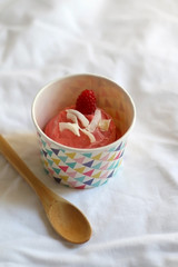 Strawberry vegan ice cream, decorated with raspberry and coconut flakes, in colorful paper cup. Top view.