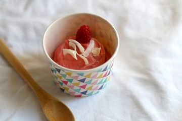 Strawberry vegan ice cream, decorated with raspberry and coconut flakes, in colorful paper cup. Top view.