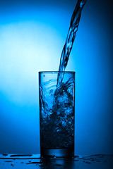 Fresh water with bubbles pours into the glass on a blue background