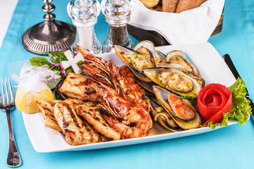 European cuisine, Mediterranean dish. Plate with assorted sea grill. Fried fish, king prawns with lemon, mussels with oyster sauce, colmar rings, crab meat